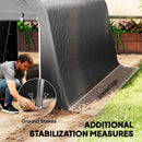 Man setting up a 10 x 15ft grey portable shed ground cover with extended edges and ground stakes on a grassy area.