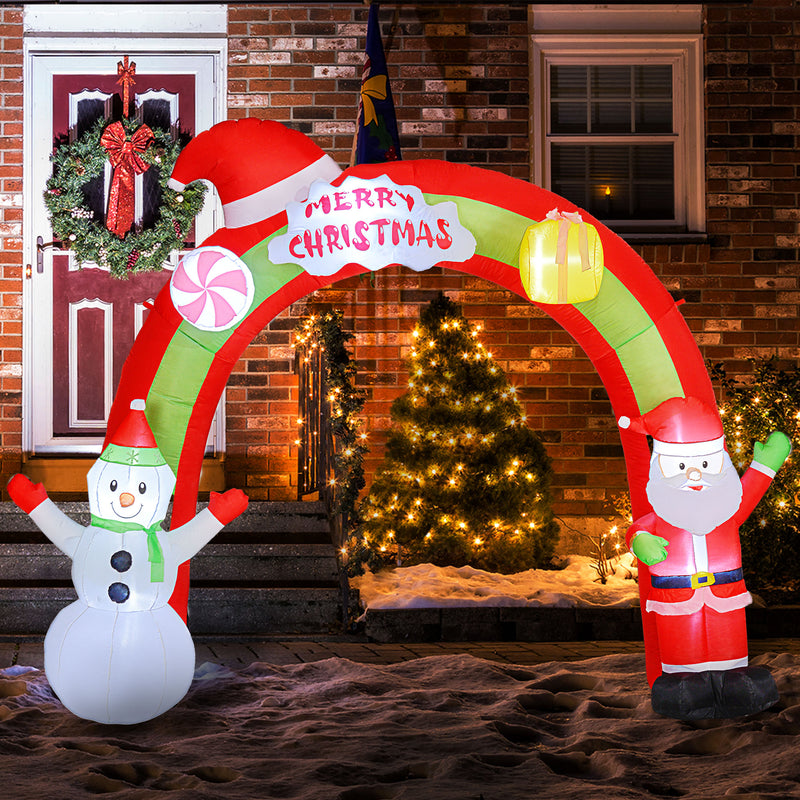 Inflatable Christmas arch with Santa Claus and snowman design in front of a house with a wreath and Christmas tree.