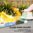 Glass wind guard in front of a propane fire pit with flames and a cup of coffee on a table.
