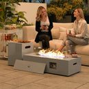 Two women sitting on a couch with a fire pit table in front of them, surrounded by plants and outdoor furniture.