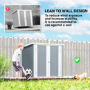 Gray metal storage shed with a child playing soccer and a dog in a grassy area, leaning against a wall.