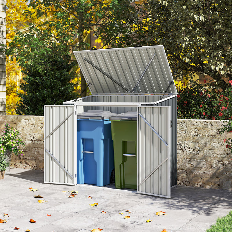 Outdoor storage shed with open lid containing blue and green trash bins, surrounded by trees and a stone wall.