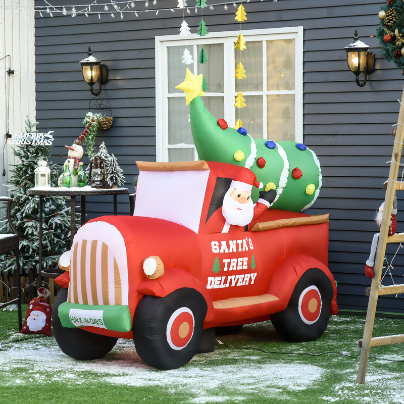 Large Christmas inflatable display  scene with a red truck carrying a decorated tree, set against a house exterior.