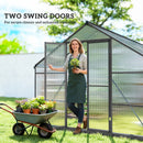 Woman standing in a greenhouse with two swing doors, holding a plant, with a wheelbarrow of potted plants nearby.