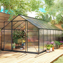 8 x 16 Greenhouse with plants on a wooden deck, surrounded by trees and garden elements.