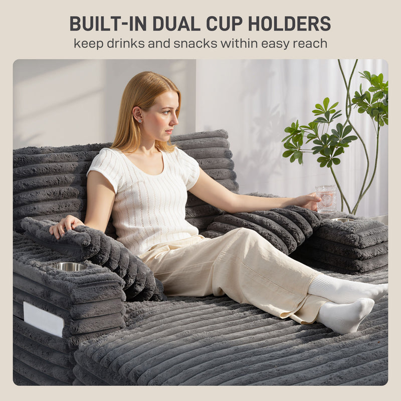 Woman sitting on a gray sofa with built-in cup holders, holding a glass.