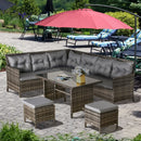 Outdoor patio furniture set with grey cushions and a red umbrella on a stone patio.