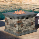 Stone finish propane MGO fire pit table with flames by a pool and patio furniture