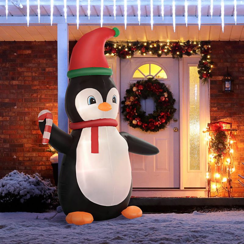 Inflatable Christmas display penguin with a candy cane in front of a house decorated for Christmas.