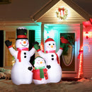 Inflatable snowman family in front of a festively decorated house with Christmas lights and wreaths.