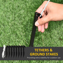 Hand holding a black ground stake with tethers on grass, labeled 'Tethers & Ground Stakes'.