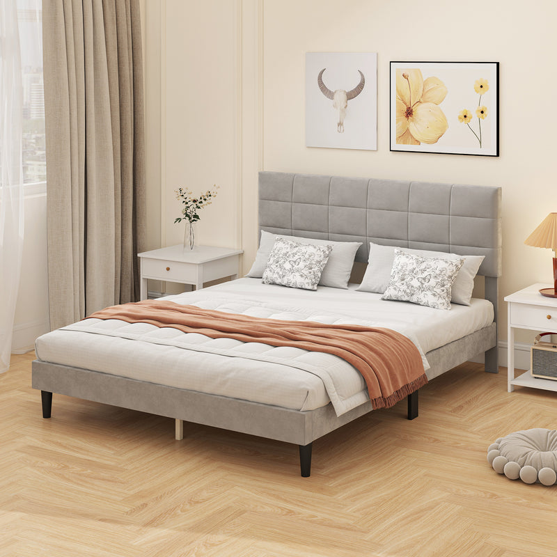 Neatly made bed with gray upholstered headboard in a bedroom setting.