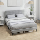 Gray upholstered bed with white bedding in a room with white walls and wooden flooring.