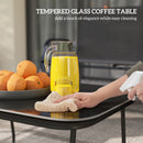 Person cleaning a tempered glass coffee table with a spray and cloth, next to a pitcher of juice and oranges.