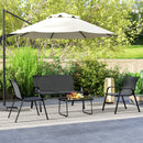 Outdoor patio set with black chairs, table, and beige umbrella on a patio with greenery in the background.