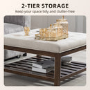 Two-tier storage coffee table with tufted upholstered top with books and decorative jars displayed on a neutral background