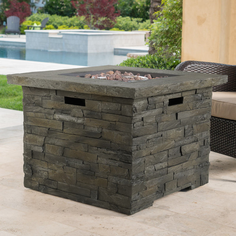 Stone-patterned outdoor fire pit table on a patio with pool and chairs in the background