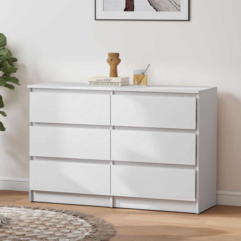 White dresser with six drawers in a room with a plant and framed picture on the wall.