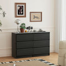 Black dresser in a bedroom with decor elements like a plant, clock, and small table.