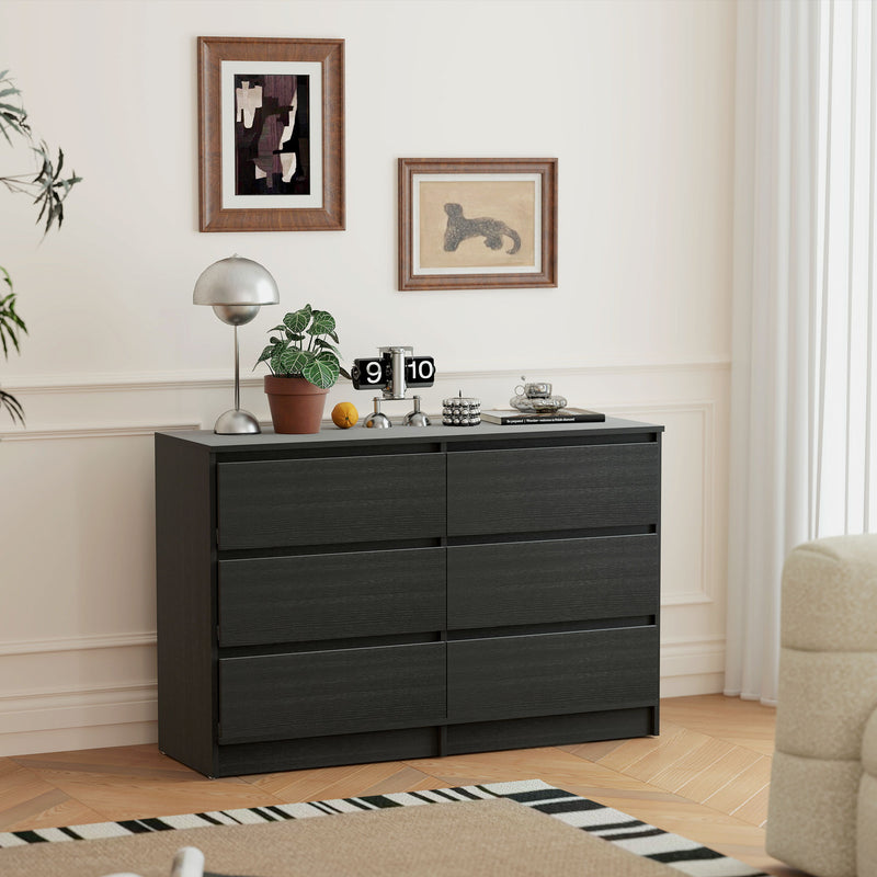 Black dresser in a bedroom with decor elements like a plant, clock, and small table.
